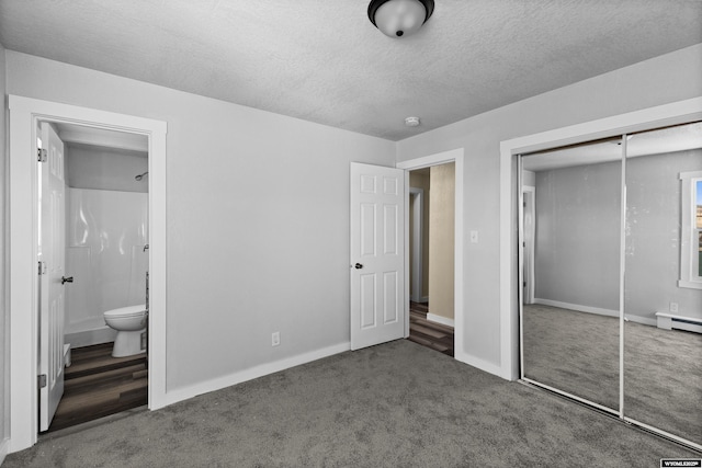 unfurnished bedroom featuring dark carpet, a baseboard heating unit, ensuite bathroom, a textured ceiling, and a closet