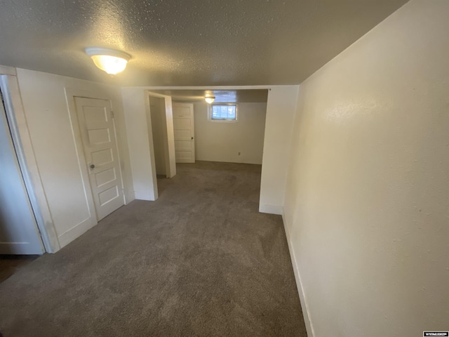 hallway with dark colored carpet and a textured ceiling