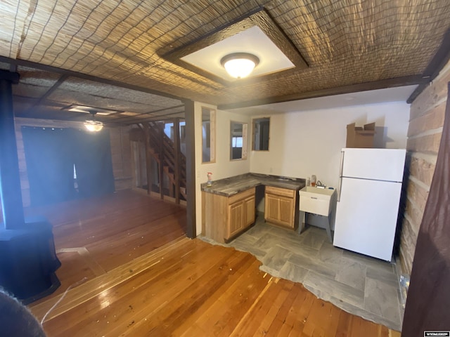 kitchen featuring hardwood / wood-style floors, white refrigerator, light brown cabinets, and brick ceiling