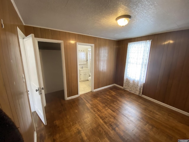 unfurnished bedroom with dark hardwood / wood-style flooring, ensuite bathroom, a textured ceiling, wooden walls, and a closet