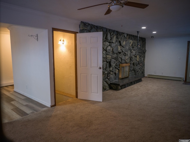 unfurnished living room featuring ceiling fan, baseboard heating, ornamental molding, and a stone fireplace