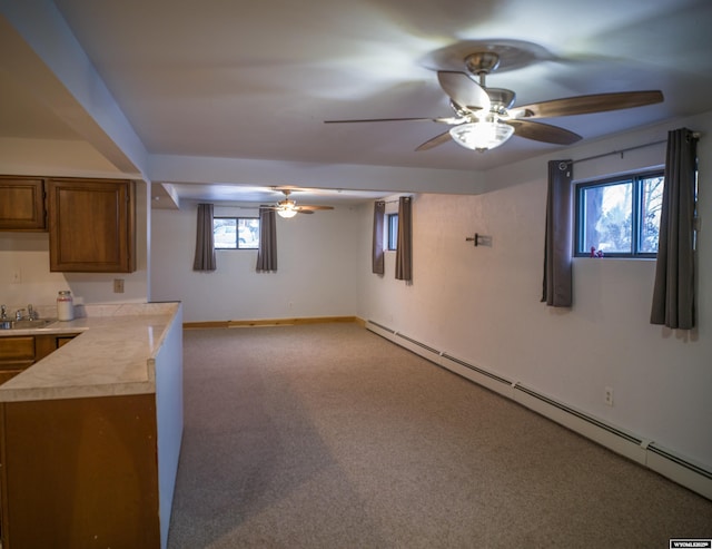 basement with ceiling fan, light colored carpet, baseboard heating, and sink