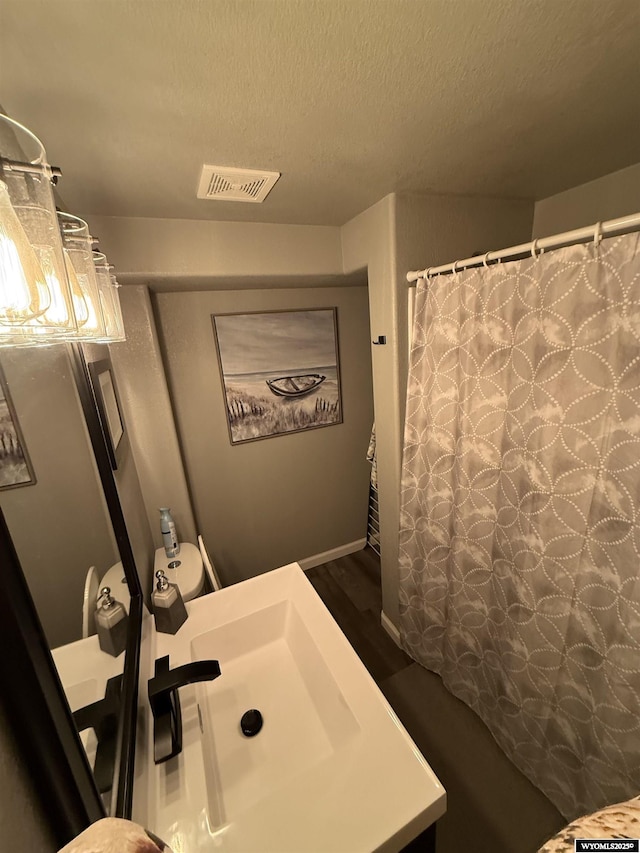 full bath with a textured ceiling, a shower with shower curtain, a sink, and visible vents