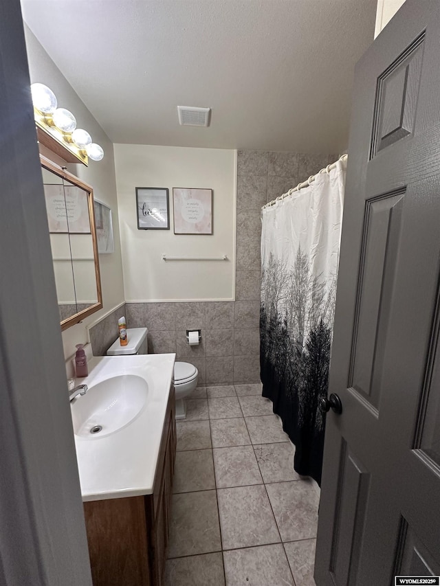 full bath with visible vents, toilet, tile patterned flooring, vanity, and tile walls