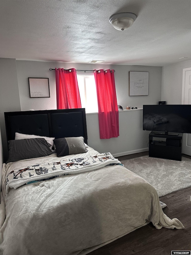 bedroom featuring visible vents, a textured ceiling, baseboards, and wood finished floors