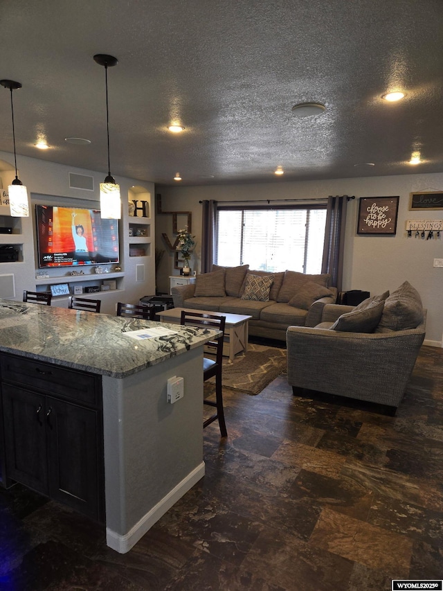 kitchen with stone counters, pendant lighting, open floor plan, and a textured ceiling