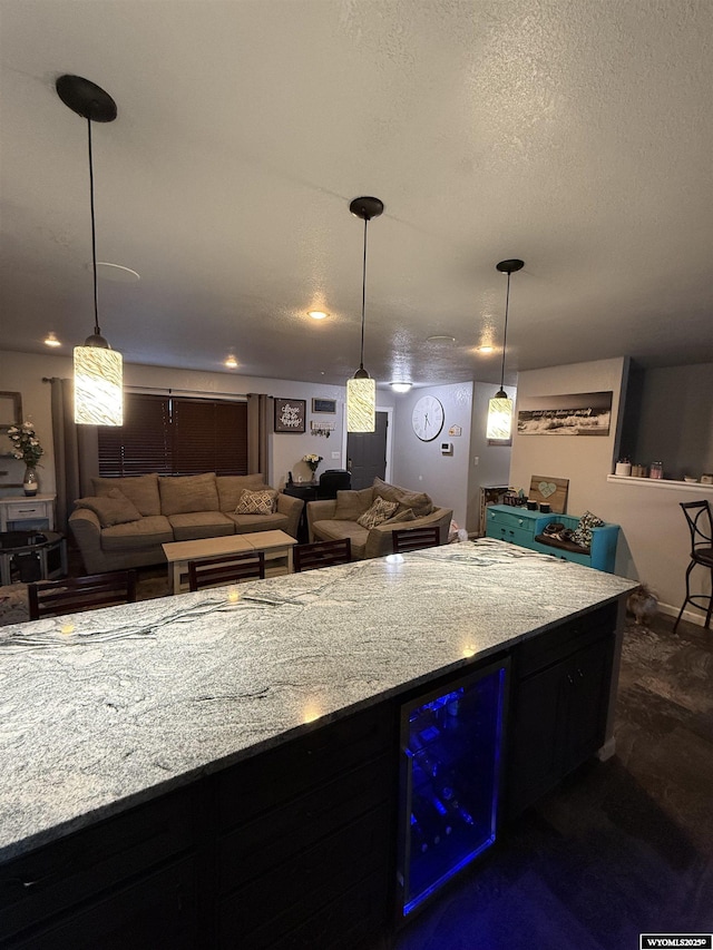 kitchen with wine cooler, light stone counters, a textured ceiling, and decorative light fixtures