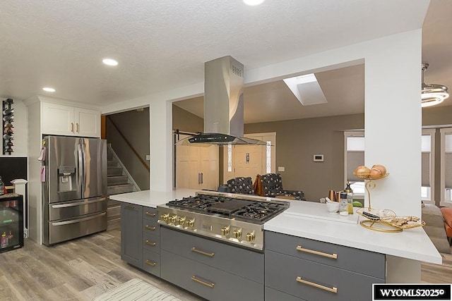 kitchen featuring wine cooler, island exhaust hood, white cabinetry, light wood-type flooring, and appliances with stainless steel finishes