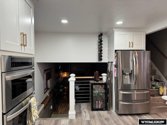 kitchen with white cabinetry, stainless steel appliances, wine cooler, wood-type flooring, and a textured ceiling