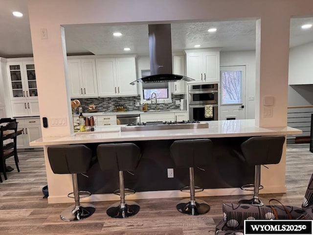 kitchen featuring island exhaust hood, white cabinetry, stainless steel appliances, and a kitchen bar