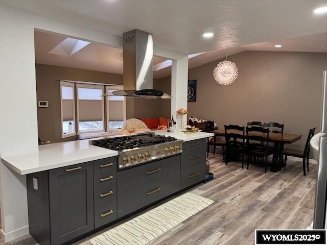 kitchen featuring vaulted ceiling, stainless steel gas cooktop, island range hood, and kitchen peninsula