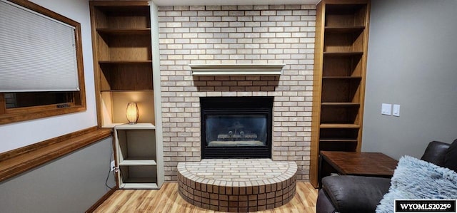 living room with a brick fireplace, light hardwood / wood-style floors, and built in features