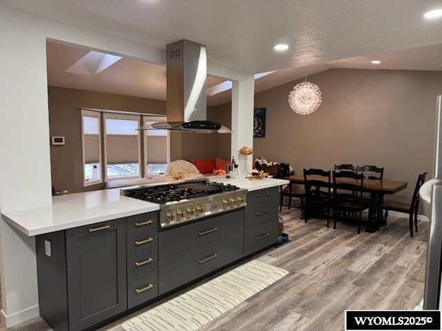 kitchen featuring kitchen peninsula, stainless steel gas cooktop, island exhaust hood, and vaulted ceiling