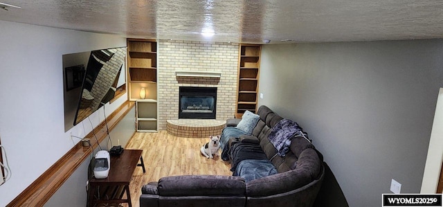 living room featuring built in shelves, wood-type flooring, a fireplace, and a textured ceiling