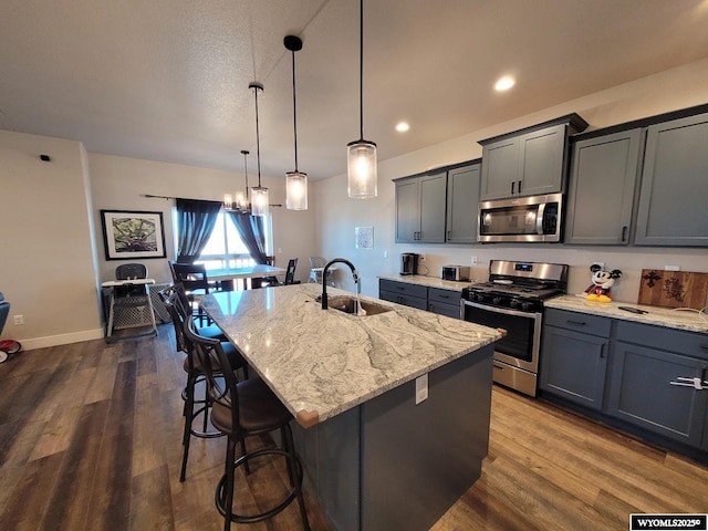 kitchen with a kitchen island with sink, sink, decorative light fixtures, and appliances with stainless steel finishes