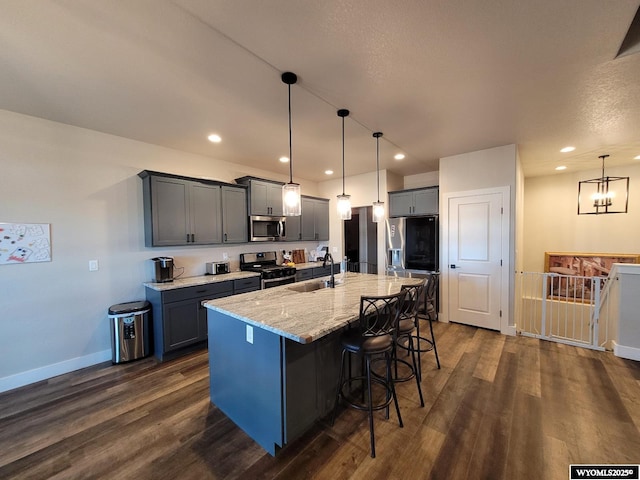 kitchen with sink, appliances with stainless steel finishes, dark hardwood / wood-style flooring, pendant lighting, and a kitchen island with sink