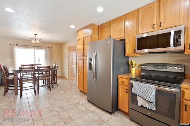 kitchen featuring light tile patterned flooring, decorative light fixtures, a notable chandelier, stainless steel appliances, and a textured ceiling