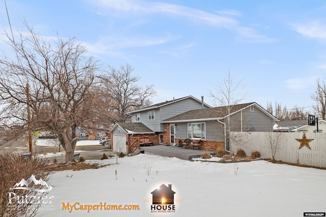 snow covered rear of property with a wooden deck and a storage unit