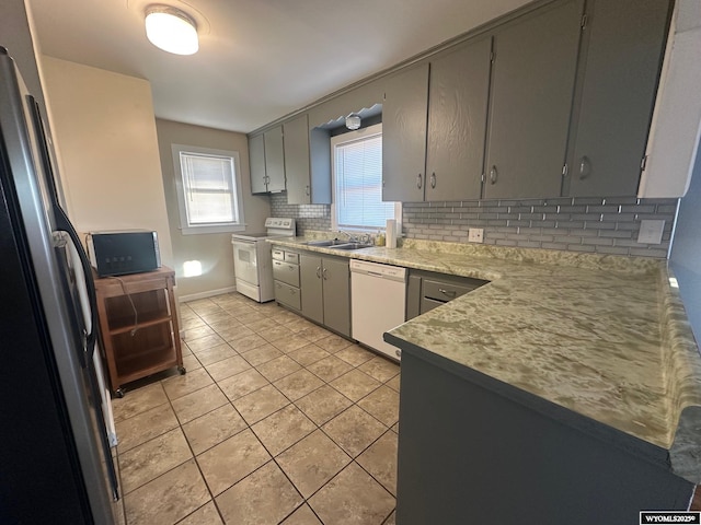 kitchen featuring light tile patterned floors, gray cabinetry, backsplash, white appliances, and sink