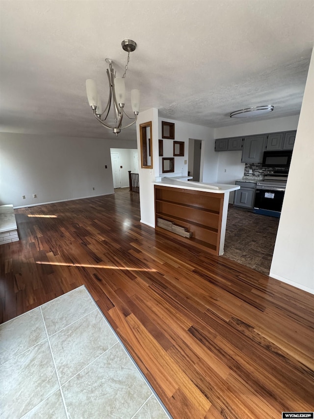 kitchen featuring dark hardwood / wood-style flooring, electric stove, backsplash, a notable chandelier, and gray cabinetry