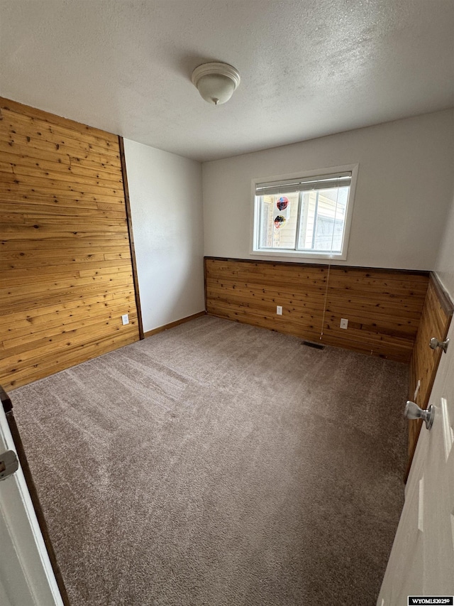 carpeted spare room featuring a textured ceiling and wood walls