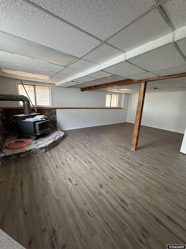 basement with a paneled ceiling, dark hardwood / wood-style flooring, and a wood stove