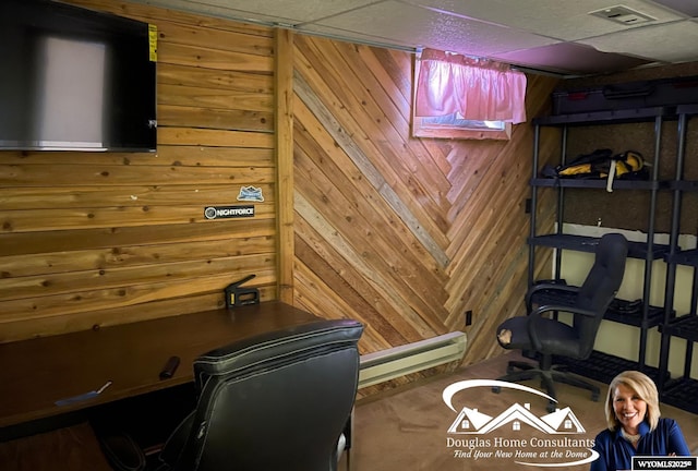 home office with a drop ceiling, wooden walls, and a baseboard heating unit