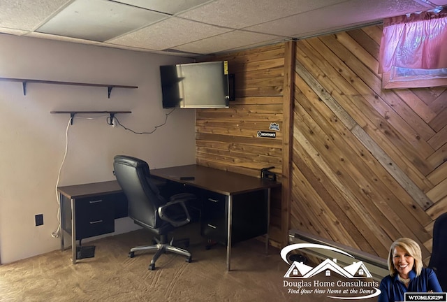 office space with carpet floors, a paneled ceiling, and wooden walls