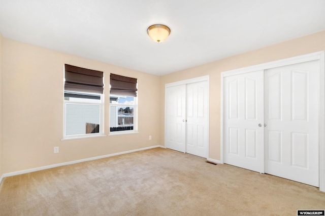 unfurnished bedroom featuring light carpet, visible vents, baseboards, and two closets