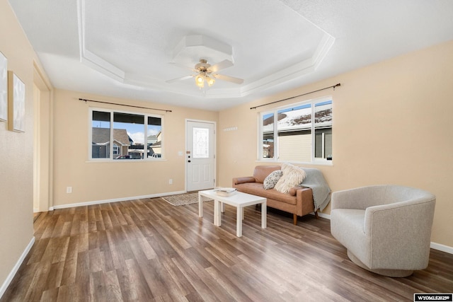 living room with a ceiling fan, a tray ceiling, baseboards, and wood finished floors