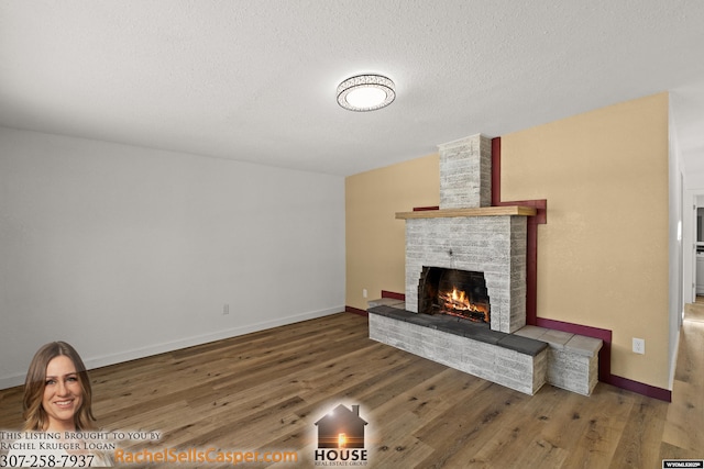 living room with a brick fireplace, a textured ceiling, and hardwood / wood-style flooring