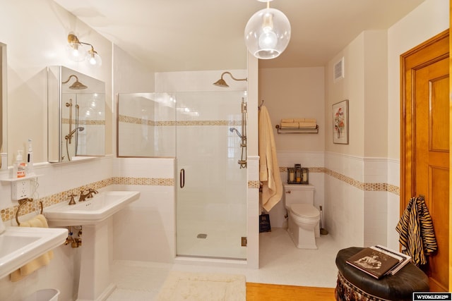 bathroom featuring toilet, a shower with shower door, tile patterned floors, and tile walls