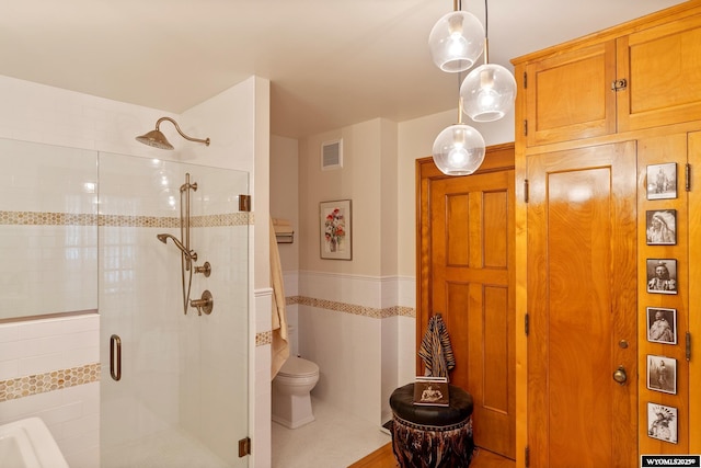 bathroom with tile walls, toilet, a shower with door, and tile patterned flooring