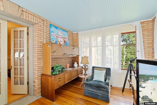 living area with wood-type flooring and brick wall