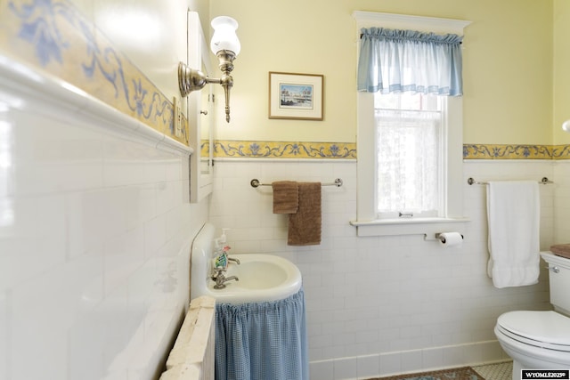 bathroom with toilet, a wealth of natural light, and tile walls