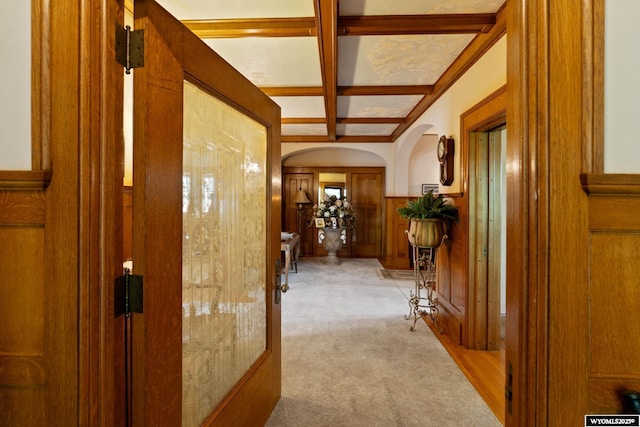 hallway with light carpet, coffered ceiling, wooden walls, and beam ceiling