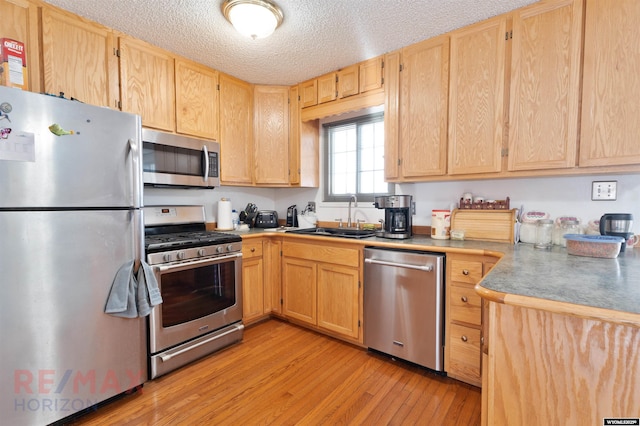 kitchen with appliances with stainless steel finishes, sink, light brown cabinets, and light hardwood / wood-style floors