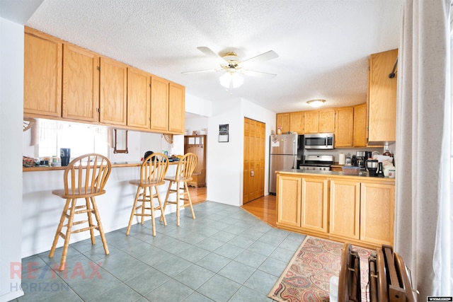 kitchen with ceiling fan, stainless steel appliances, a kitchen breakfast bar, and light brown cabinetry