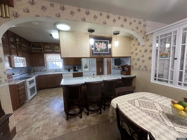 kitchen featuring pendant lighting, sink, white appliances, and a kitchen bar