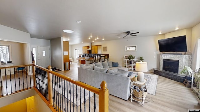 living room featuring ceiling fan, a tile fireplace, and light wood-type flooring