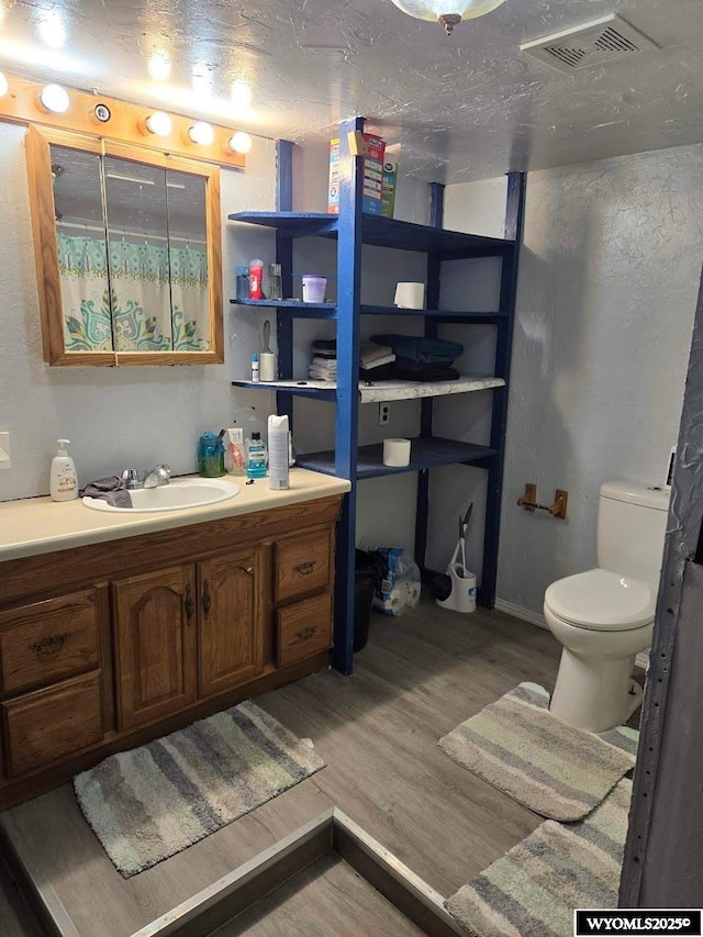 bathroom with visible vents, toilet, a textured ceiling, vanity, and wood finished floors