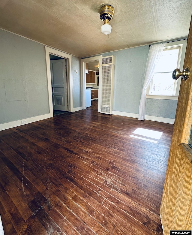 empty room with a textured ceiling, dark wood finished floors, and baseboards