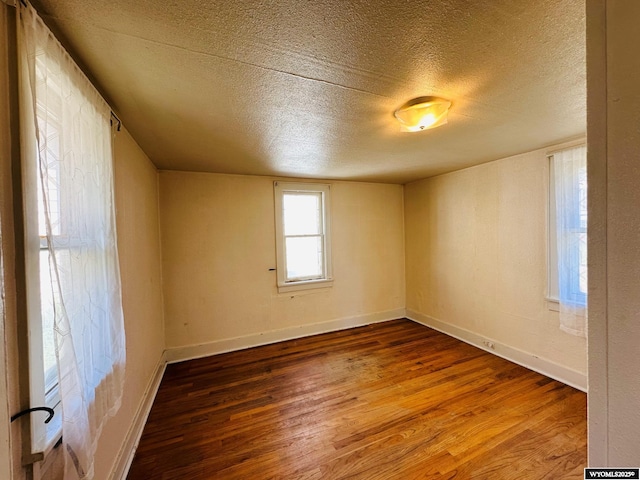 spare room with a textured ceiling, wood finished floors, and baseboards