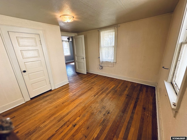 unfurnished room featuring dark wood-style flooring, a textured ceiling, and baseboards