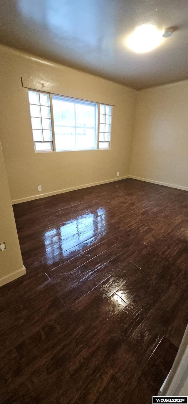 unfurnished room featuring dark wood-style floors, plenty of natural light, and baseboards