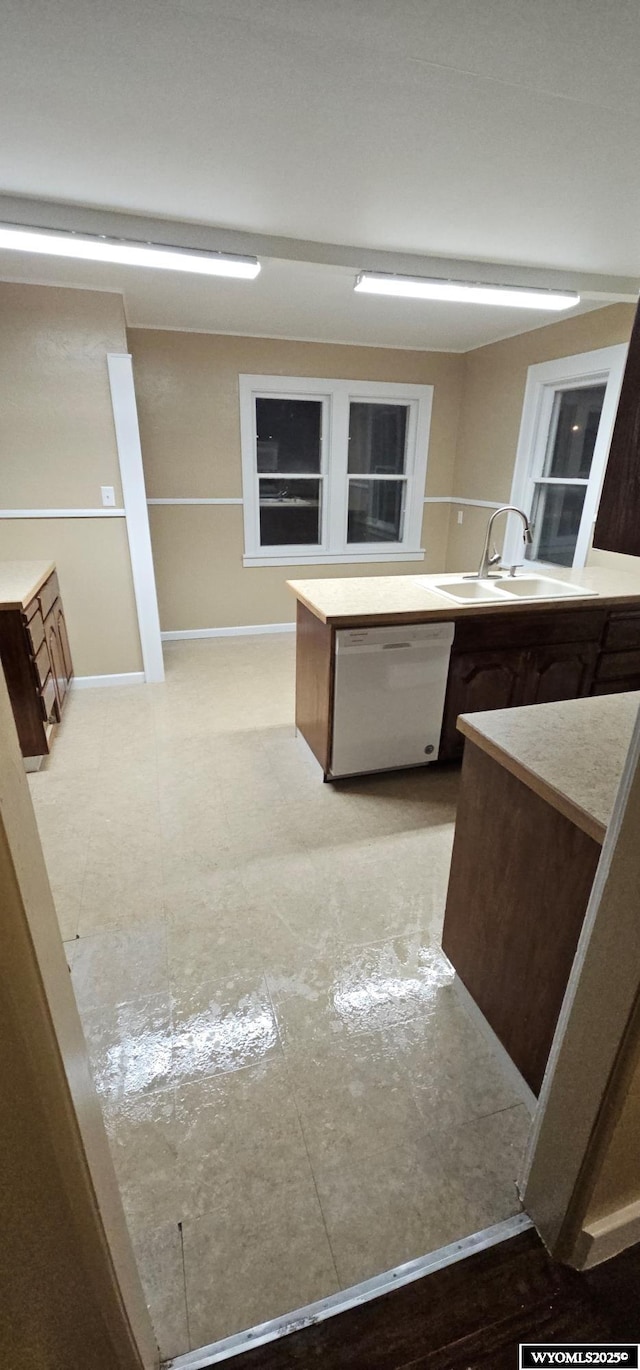 kitchen featuring white dishwasher, baseboards, and a sink