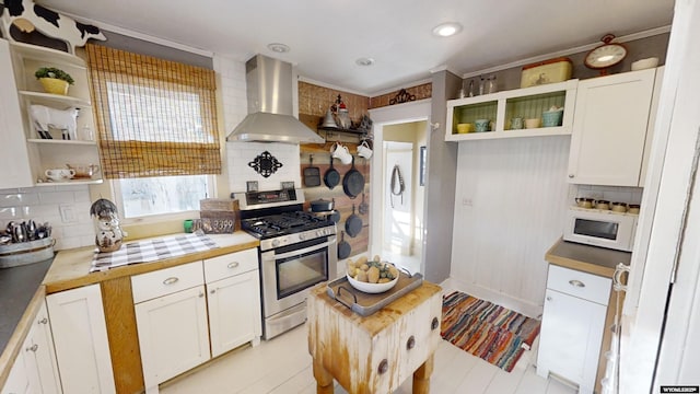 kitchen with tasteful backsplash, stainless steel range with gas stovetop, wall chimney range hood, and white cabinets