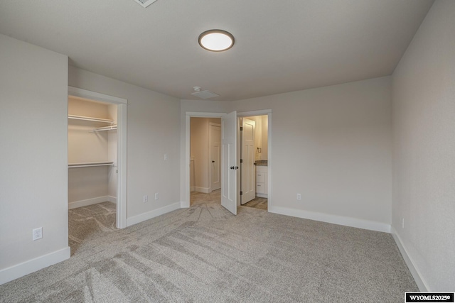 unfurnished bedroom with a spacious closet, light carpet, ensuite bath, and a closet
