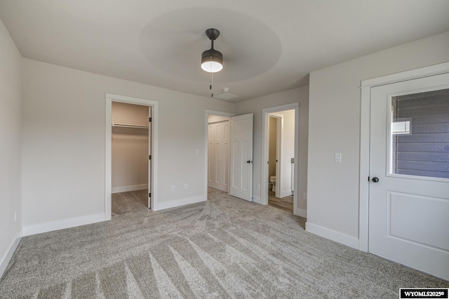 unfurnished bedroom with light carpet, a walk in closet, and ceiling fan