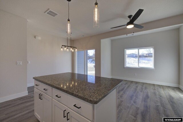kitchen featuring hanging light fixtures, a kitchen island, dark stone countertops, and white cabinets